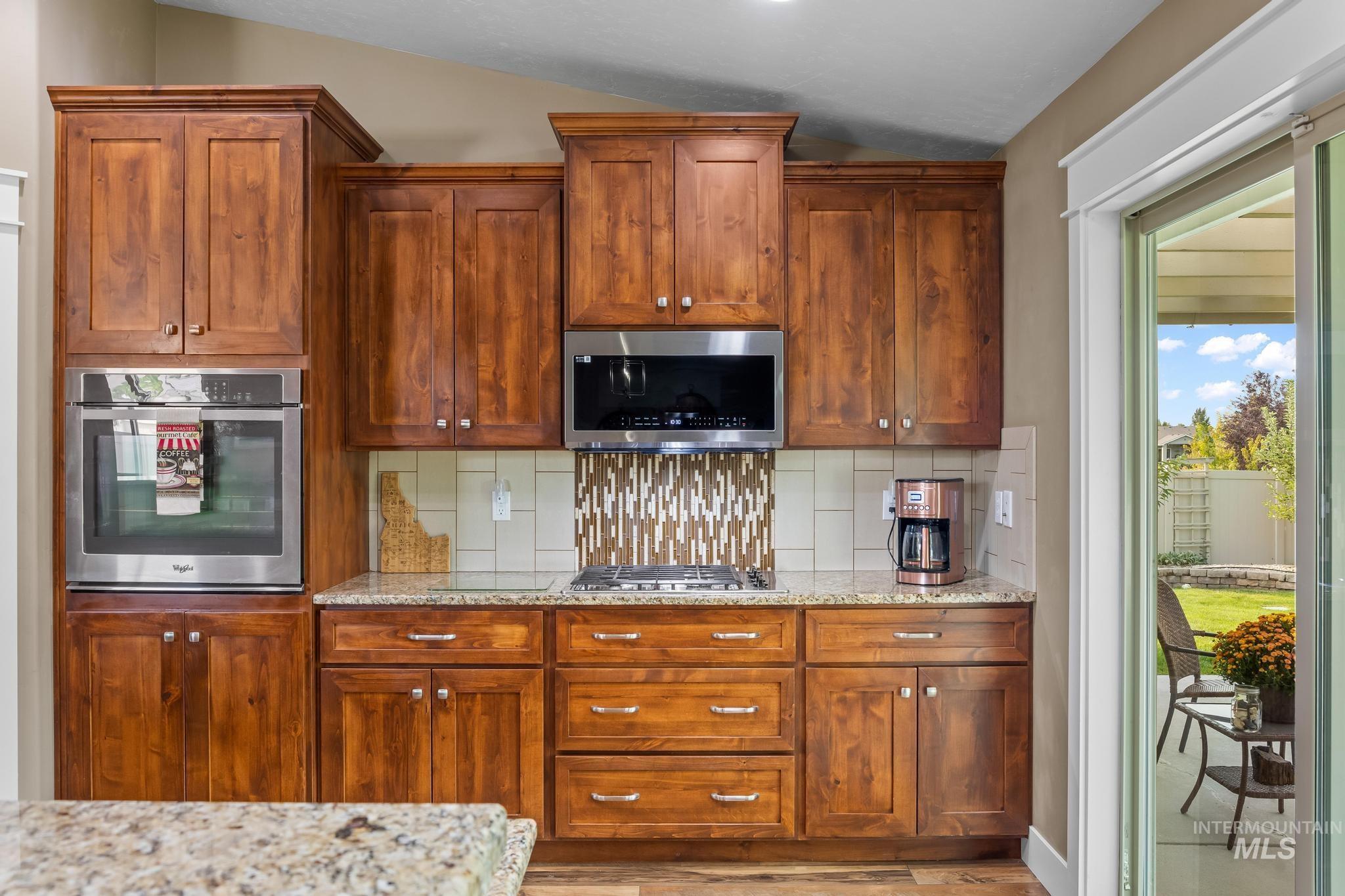 Kitchen featuring decorative backsplash, appliances with stainless steel finishes, light stone countertops, and brown cabinets