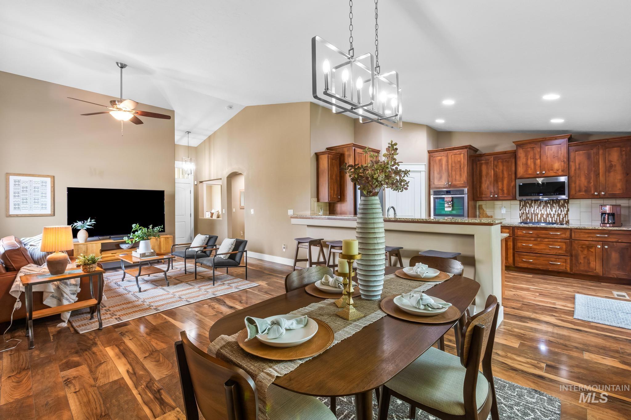 Dining space featuring dark wood finished floors, ceiling fan, high vaulted ceiling, arched walkways, and a chandelier