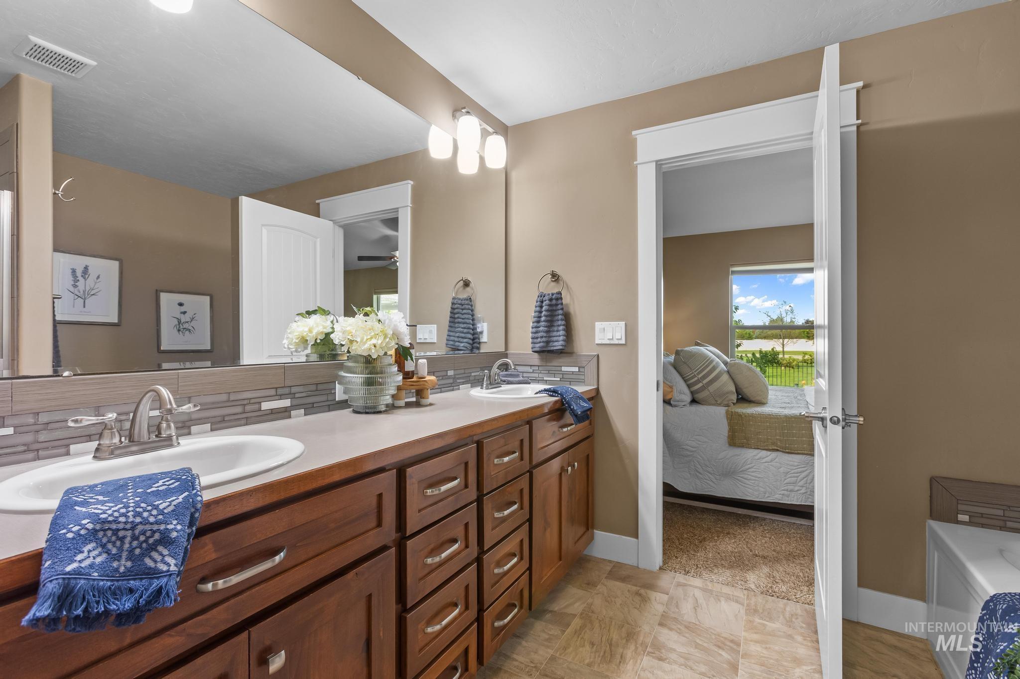 Ensuite bathroom featuring double vanity, a bath, backsplash, and a ceiling fan