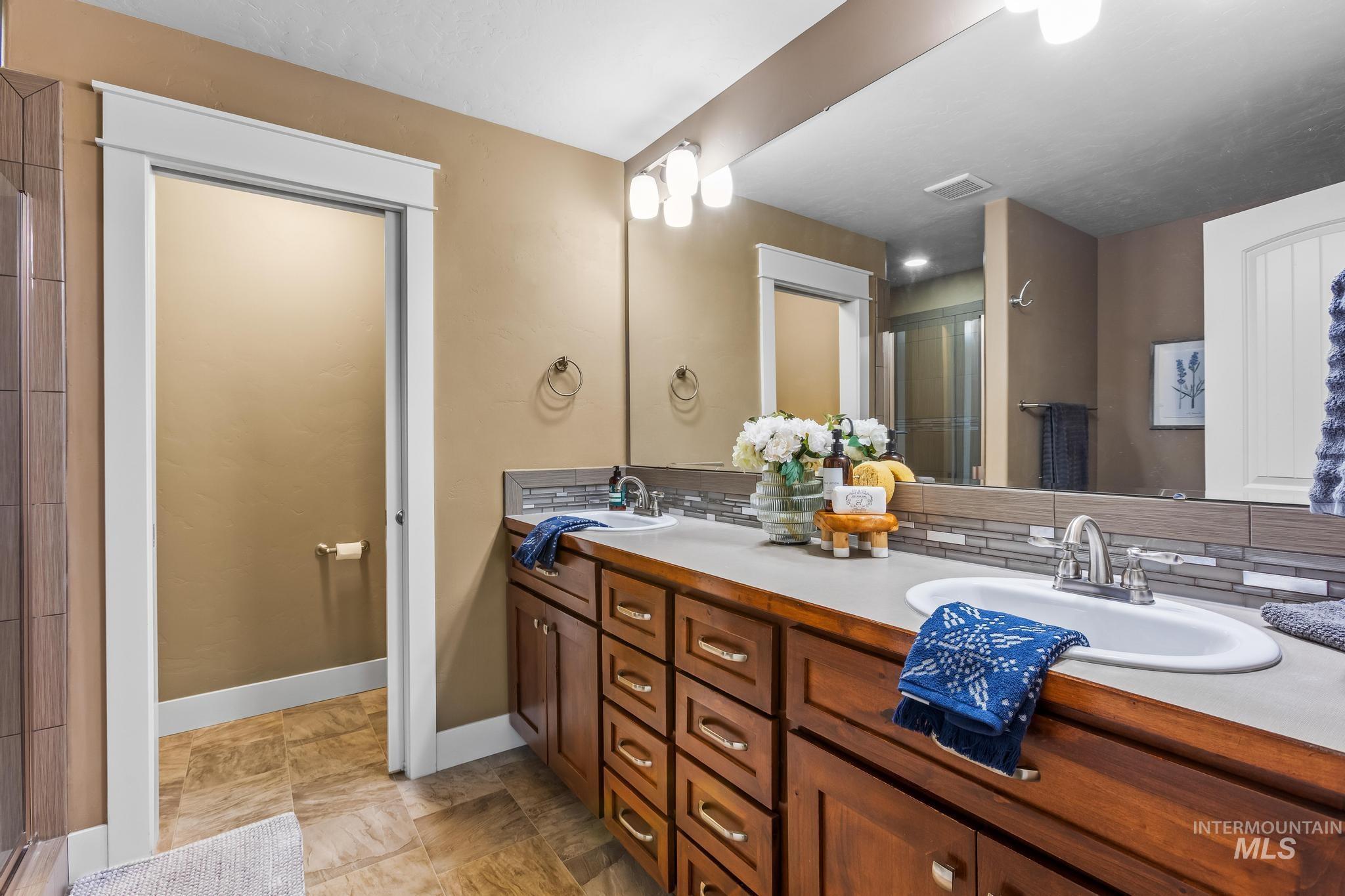 Bathroom featuring double vanity, a stall shower, and backsplash