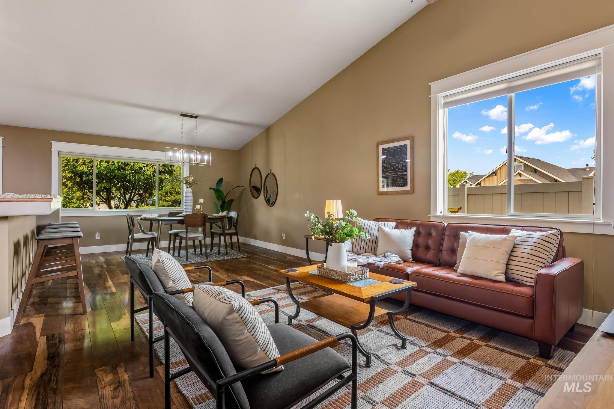 Living area with dark wood-type flooring, plenty of natural light, vaulted ceiling, and a chandelier