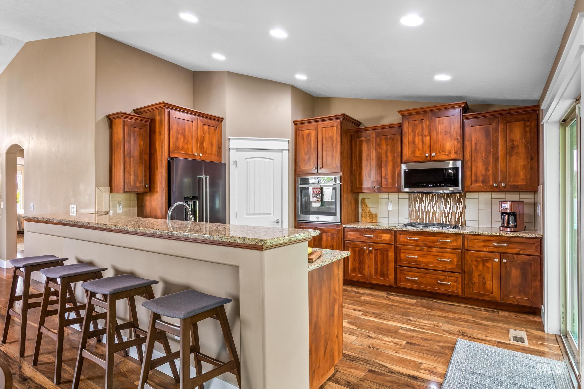 Kitchen featuring vaulted ceiling, tasteful backsplash, a breakfast bar, light stone counters, and a peninsula