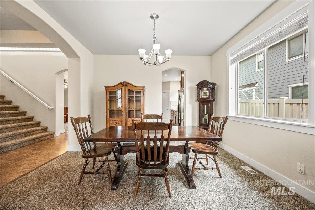 Carpeted dining room featuring arched walkways, stairway, and a chandelier