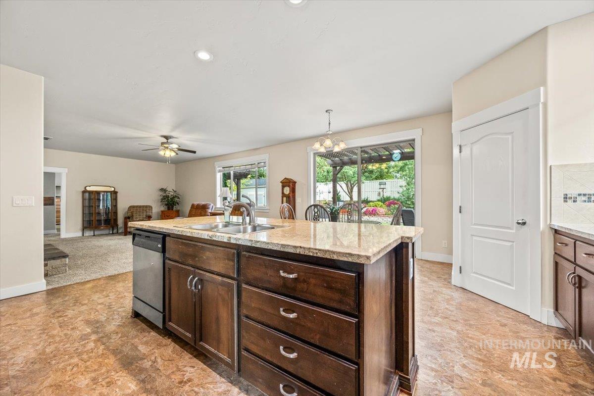 Kitchen with dark brown cabinetry, recessed lighting, an island with sink, hanging light fixtures, and light stone countertops