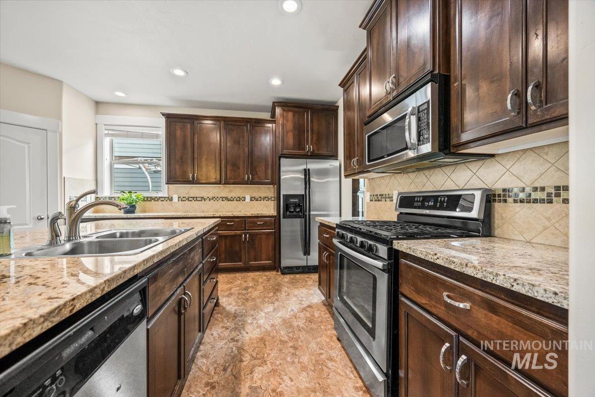 Kitchen featuring appliances with stainless steel finishes, dark brown cabinetry, backsplash, recessed lighting, and light stone countertops