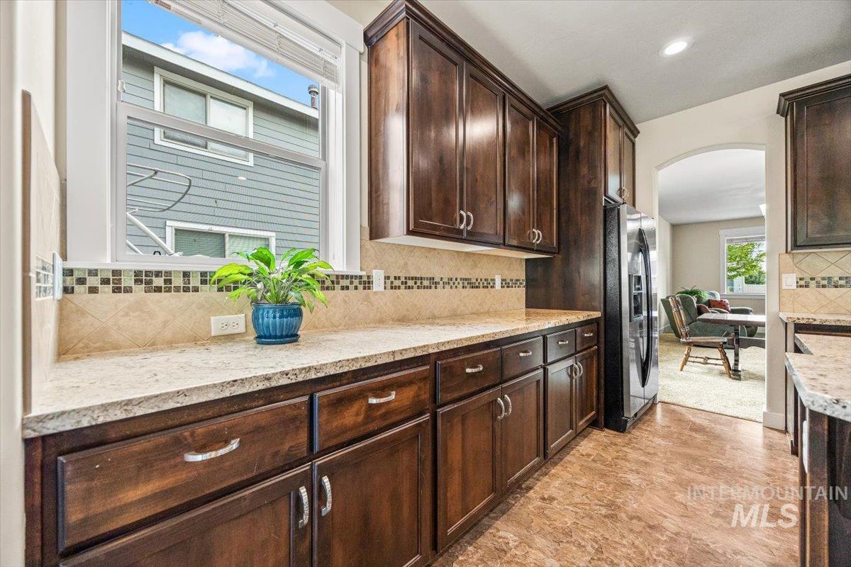 Kitchen with decorative backsplash, stainless steel fridge, dark brown cabinetry, arched walkways, and recessed lighting