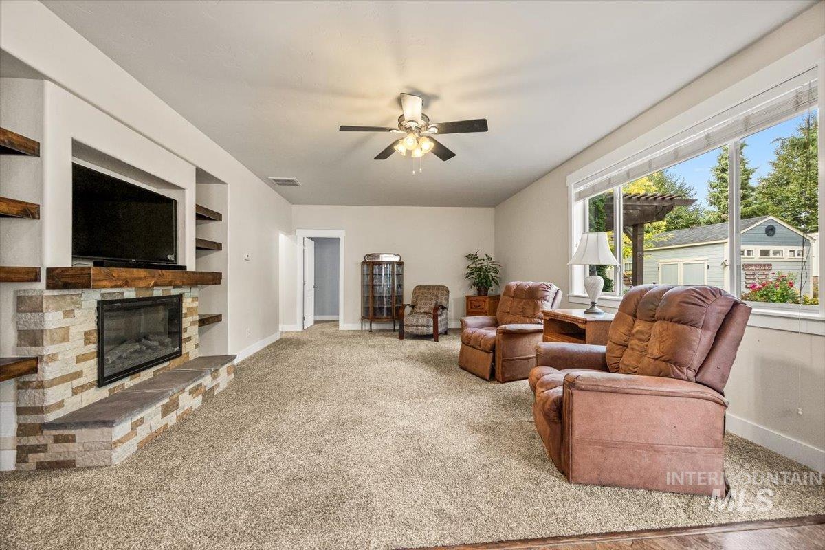 Living area featuring light carpet, a stone fireplace, ceiling fan, and built in features