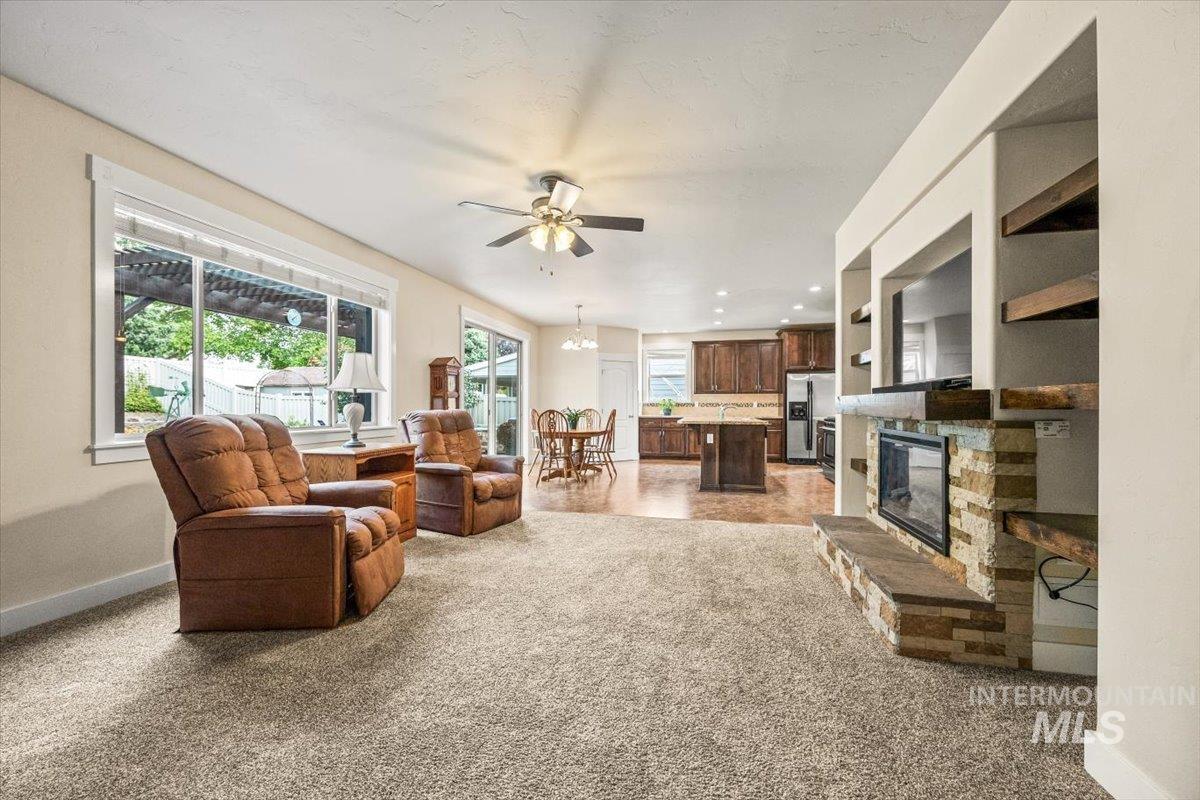 Living area with a stone fireplace, a chandelier, a ceiling fan, and light colored carpet