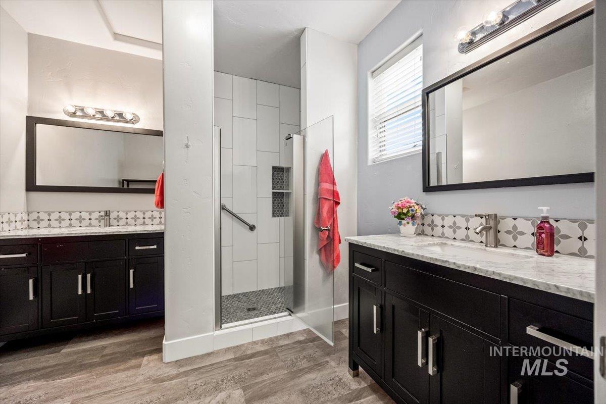 Full bathroom featuring a stall shower, two vanities, and light wood finished floors