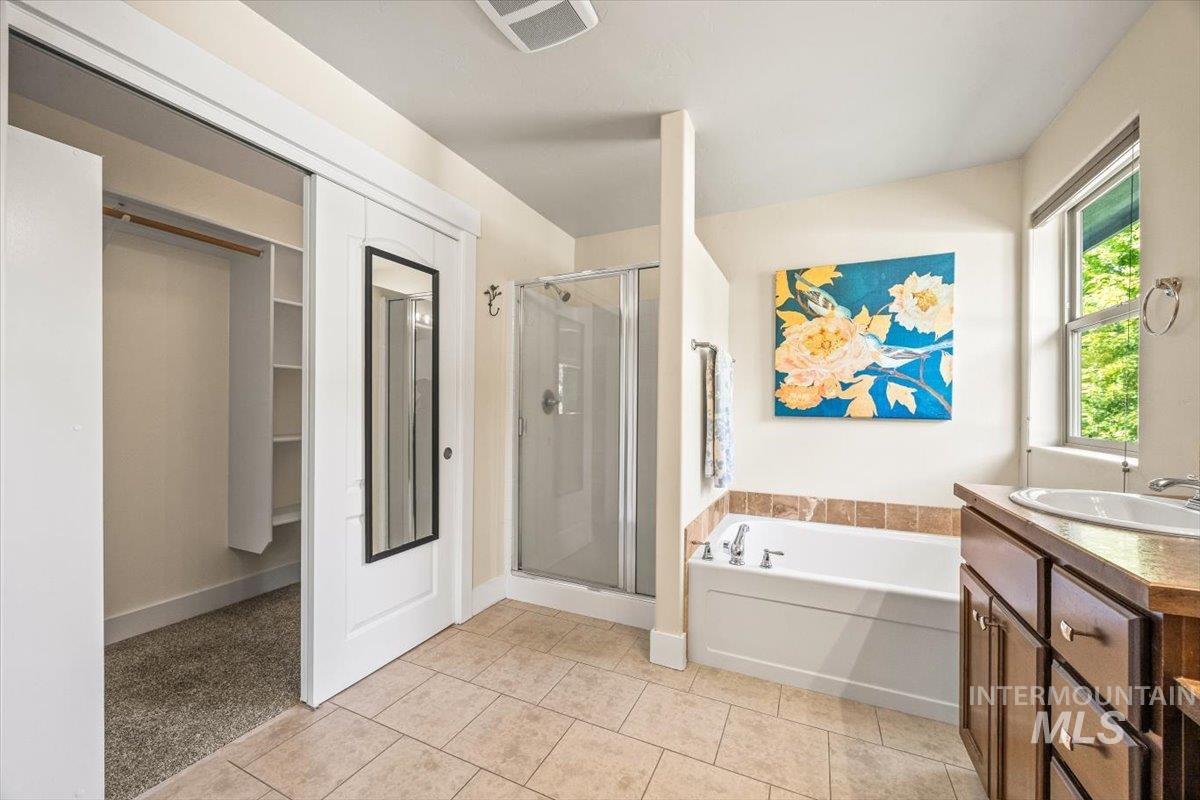 Full bathroom featuring vanity, a stall shower, a garden tub, light tile patterned flooring, and a closet