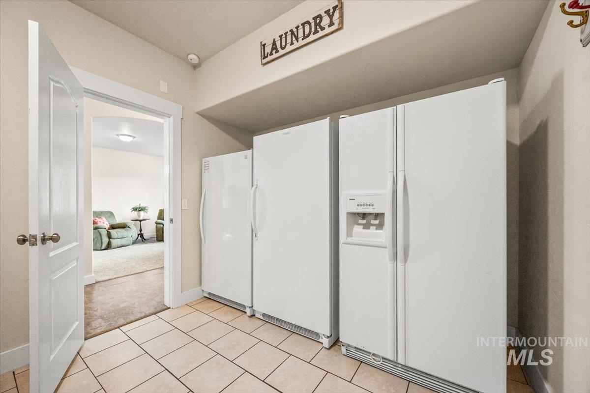 Kitchen featuring white fridge with ice dispenser, light tile patterned floors, freestanding refrigerator, and light colored carpet