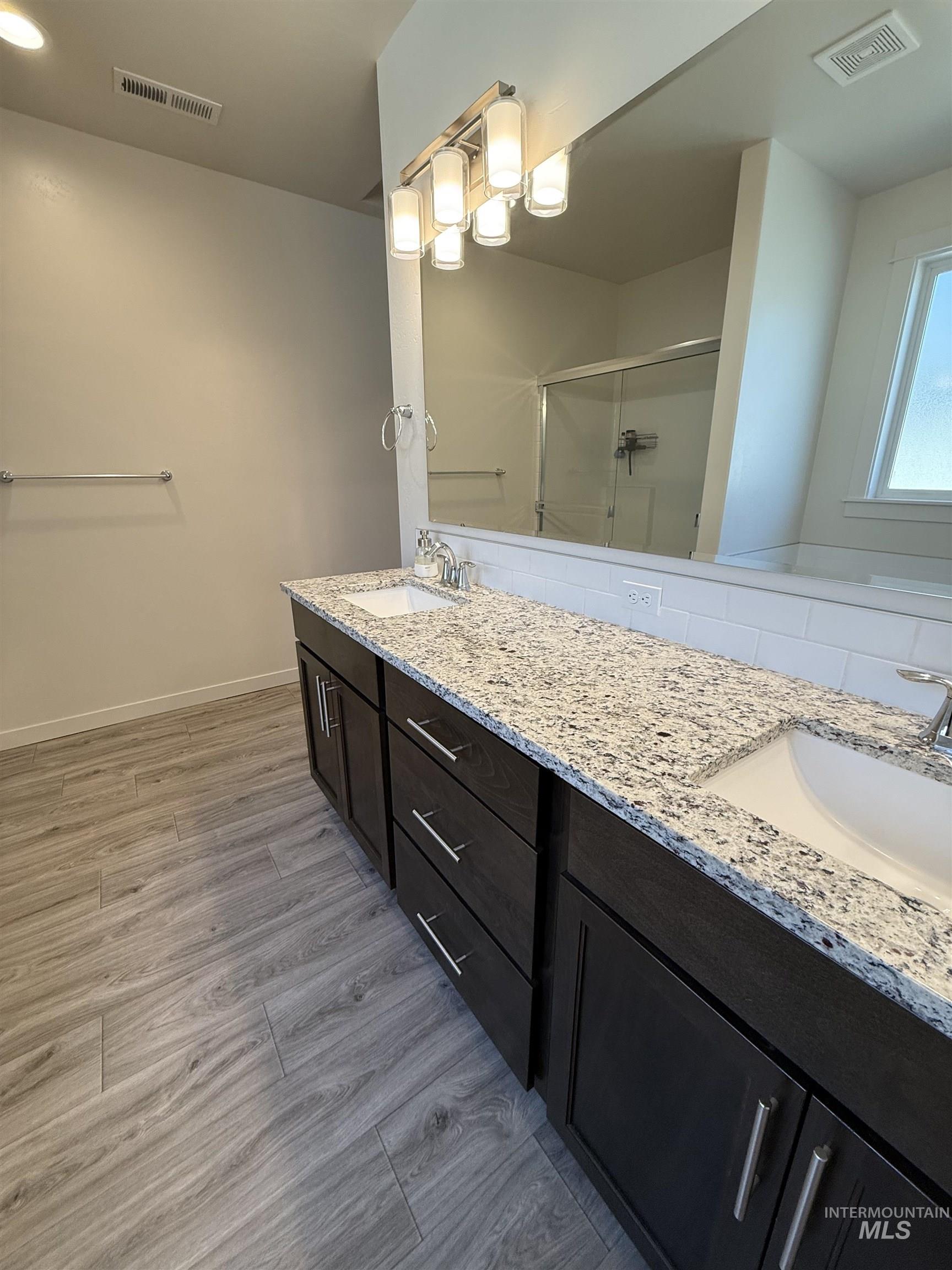 Bathroom with double vanity, a shower stall, and light wood-style flooring