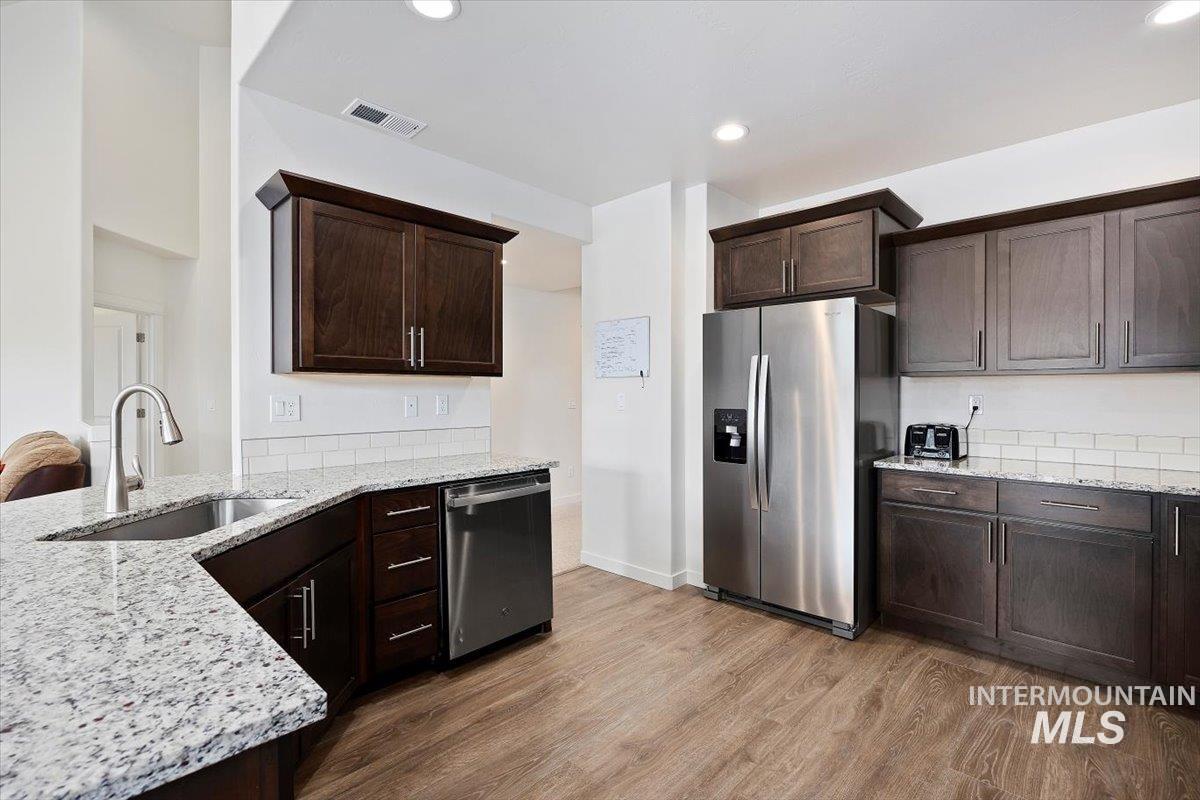 Kitchen with light stone countertops, dark brown cabinets, stainless steel appliances, and recessed lighting