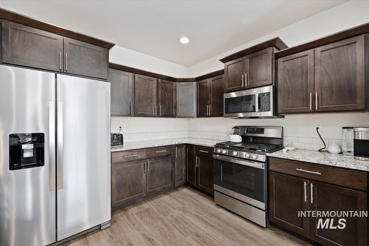 Kitchen featuring stainless steel appliances, dark brown cabinetry, light wood finished floors, light stone counters, and recessed lighting