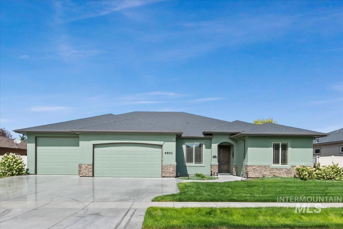 View of front facade featuring stucco siding, a garage, a front yard, driveway, and stone siding