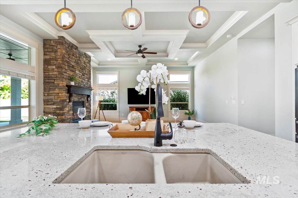 Kitchen with ceiling fan, light stone countertops, decorative light fixtures, open floor plan, and coffered ceiling