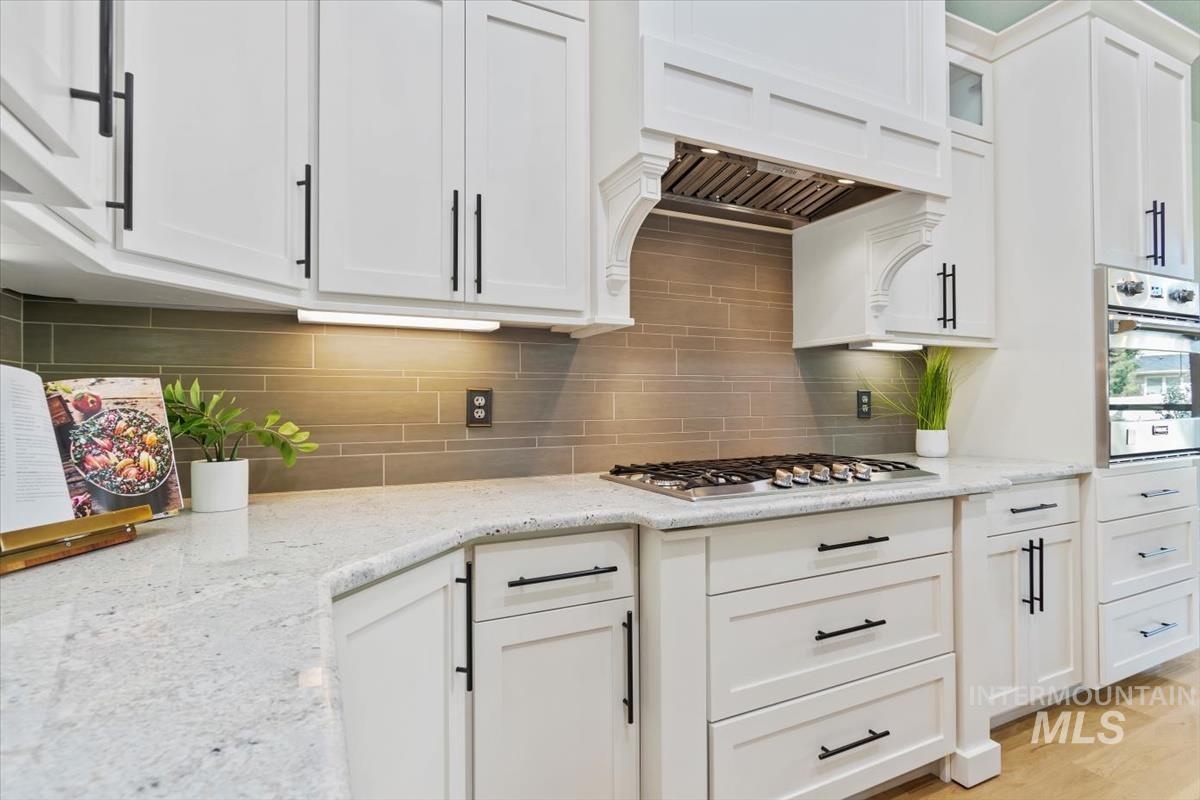 Kitchen featuring light stone counters, stainless steel appliances, white cabinets, and decorative backsplash