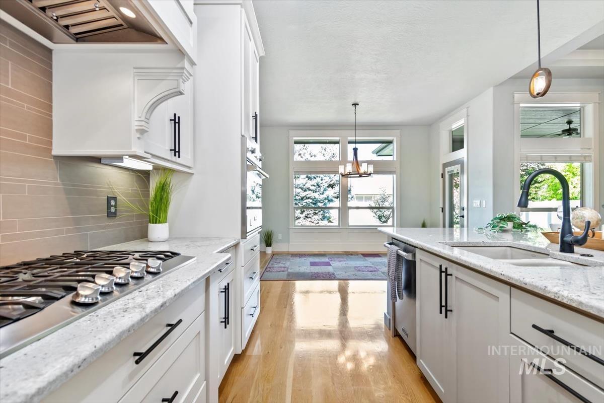 Kitchen with white cabinets, light wood-style flooring, decorative light fixtures, light stone counters, and appliances with stainless steel finishes