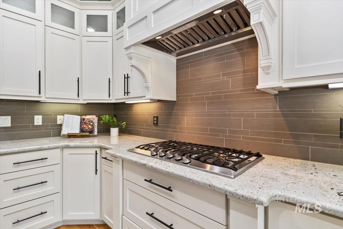 Kitchen featuring premium range hood, white cabinetry, tasteful backsplash, light stone counters, and stainless steel gas cooktop