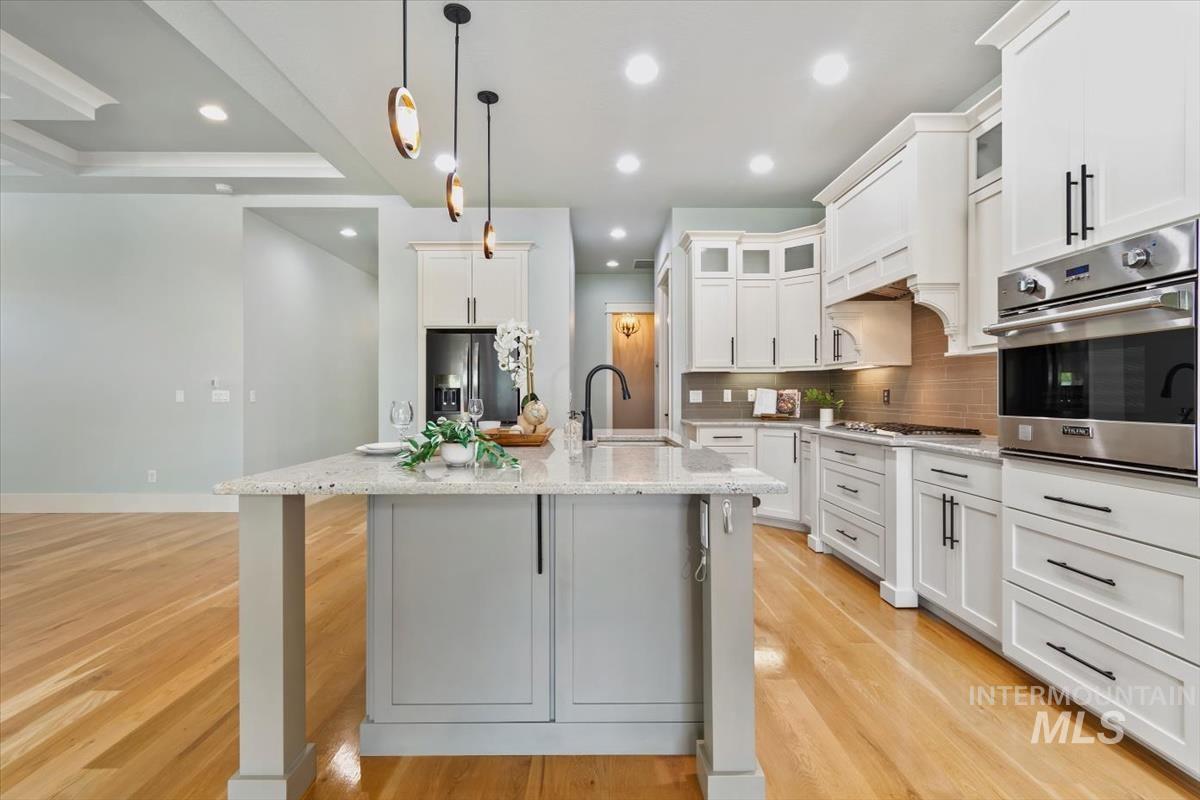 Kitchen with glass insert cabinets, stainless steel appliances, pendant lighting, light stone countertops, and a kitchen island with sink