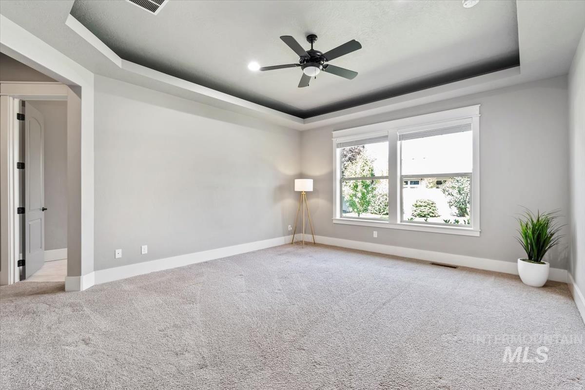 Unfurnished room with a tray ceiling, light carpet, and a ceiling fan
