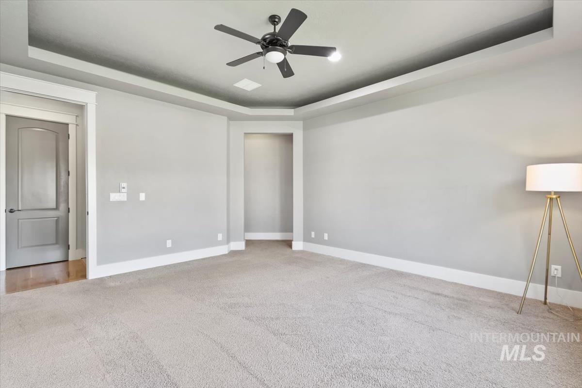 Unfurnished bedroom with a tray ceiling, light carpet, and a ceiling fan