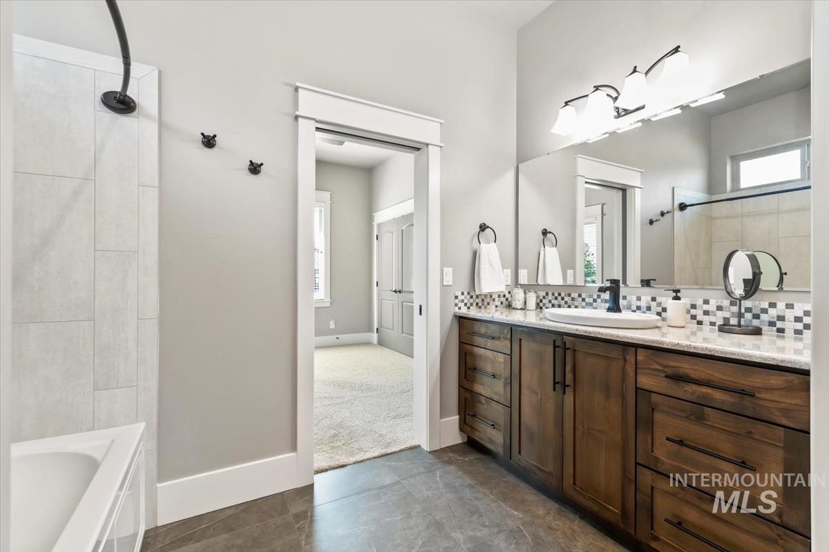Bathroom featuring vanity, decorative backsplash, dark tile patterned flooring, and tiled shower / bath