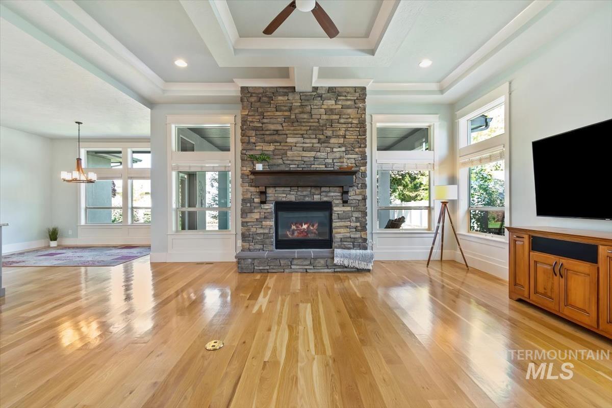 Unfurnished living room with light wood finished floors, a ceiling fan, a raised ceiling, and a stone fireplace
