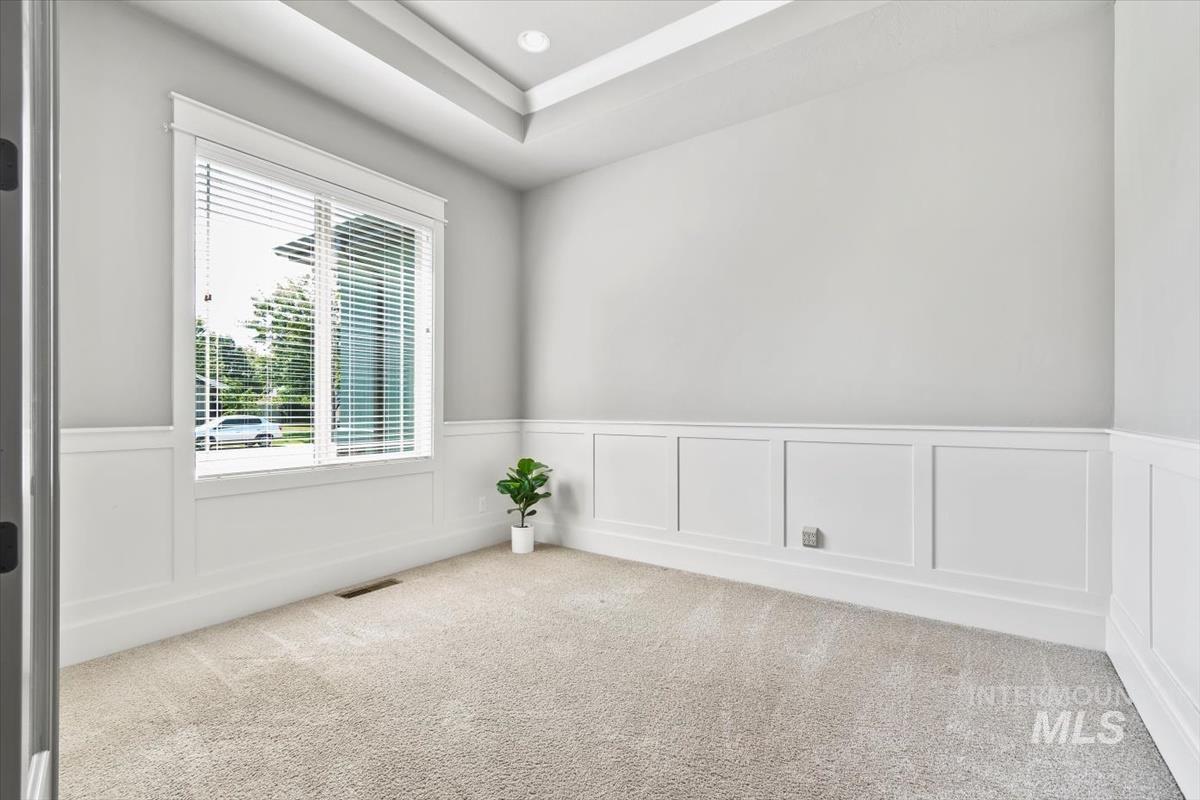 Empty room with a decorative wall, a wainscoted wall, carpet flooring, a tray ceiling, and recessed lighting