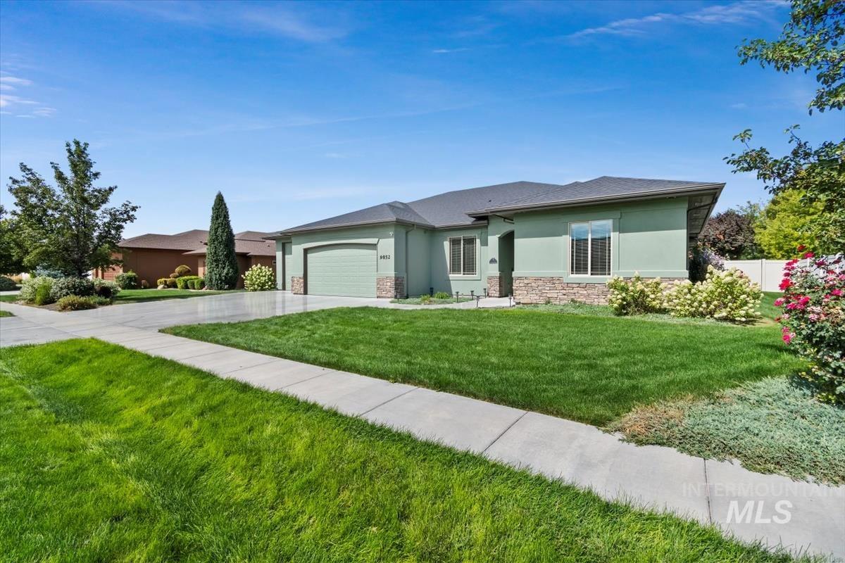 View of front of property featuring stucco siding, an attached garage, driveway, stone siding, and a front lawn