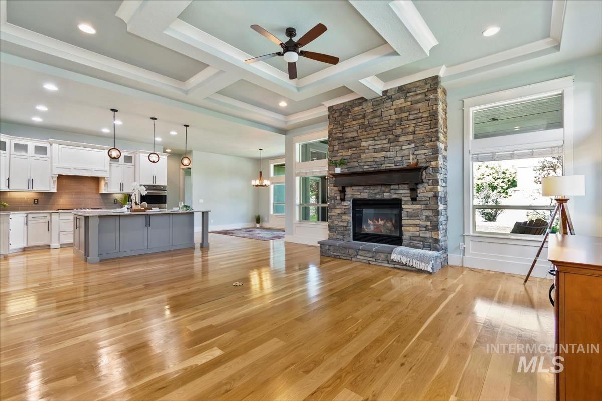 Living area with a chandelier, plenty of natural light, light wood-style flooring, a ceiling fan, and coffered ceiling