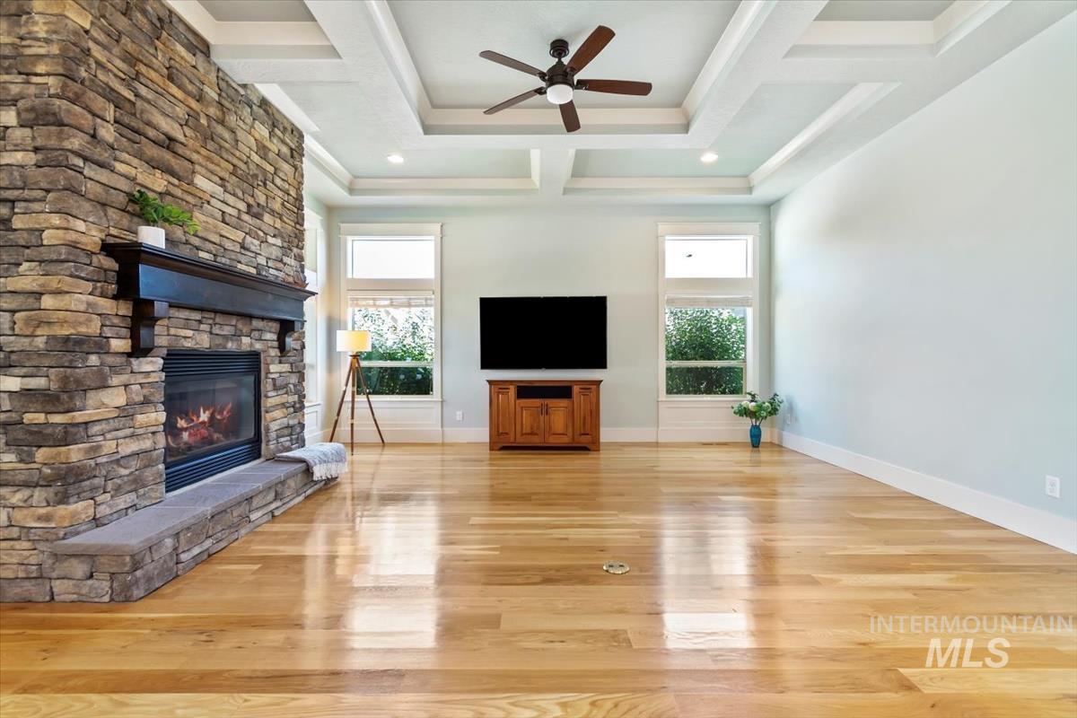 Unfurnished living room with healthy amount of natural light, light wood-style flooring, coffered ceiling, ceiling fan, and beamed ceiling