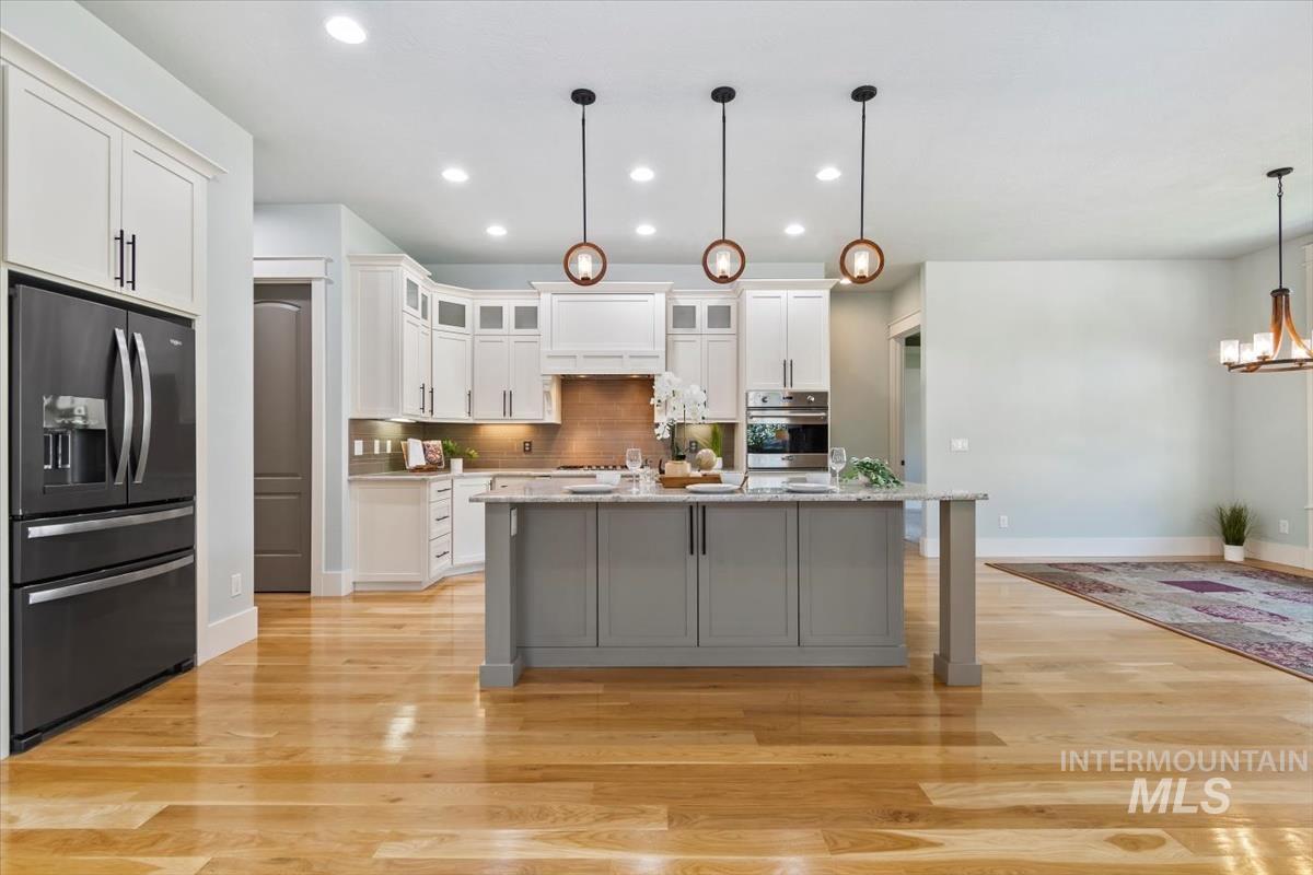 Kitchen with black fridge with ice dispenser, glass insert cabinets, decorative backsplash, white cabinetry, and recessed lighting