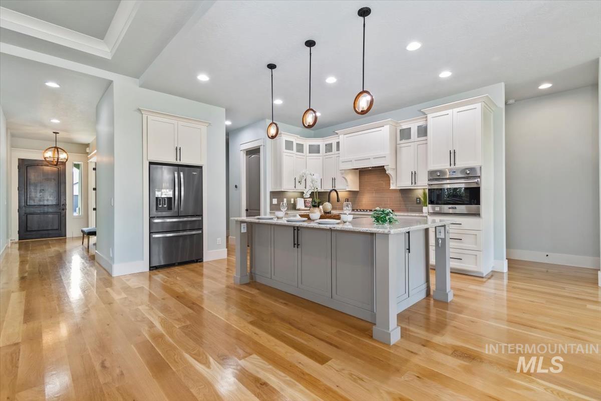 Kitchen featuring glass insert cabinets, decorative backsplash, decorative light fixtures, stainless steel appliances, and gray cabinetry