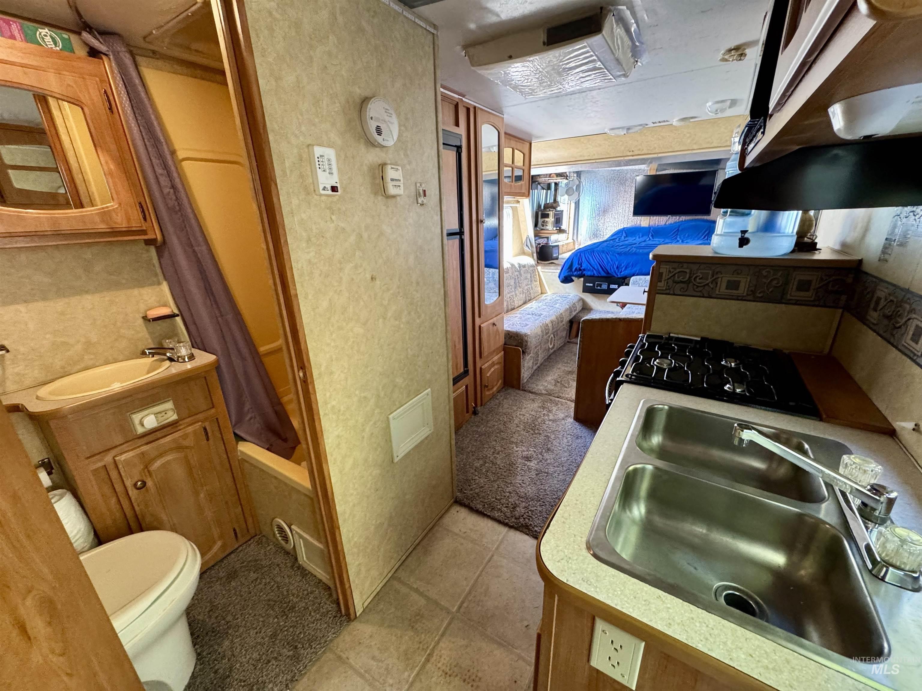 Kitchen featuring light countertops, open floor plan, light tile patterned flooring, gas stove, and brown cabinets