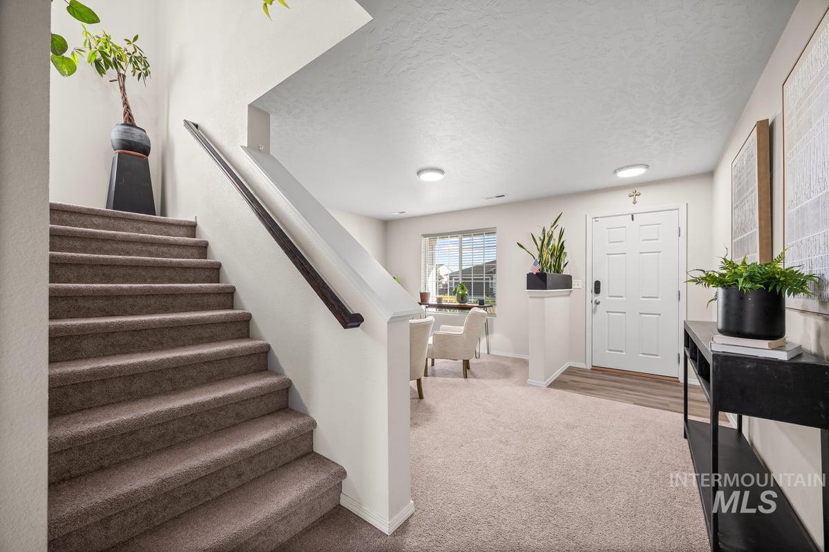Foyer entrance featuring stairs, light carpet, and a textured ceiling