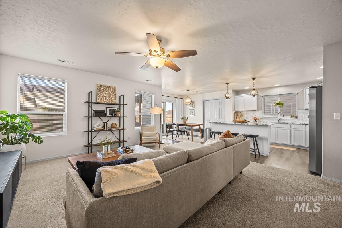 Living room featuring a textured ceiling, plenty of natural light, ceiling fan, light colored carpet, and a chandelier