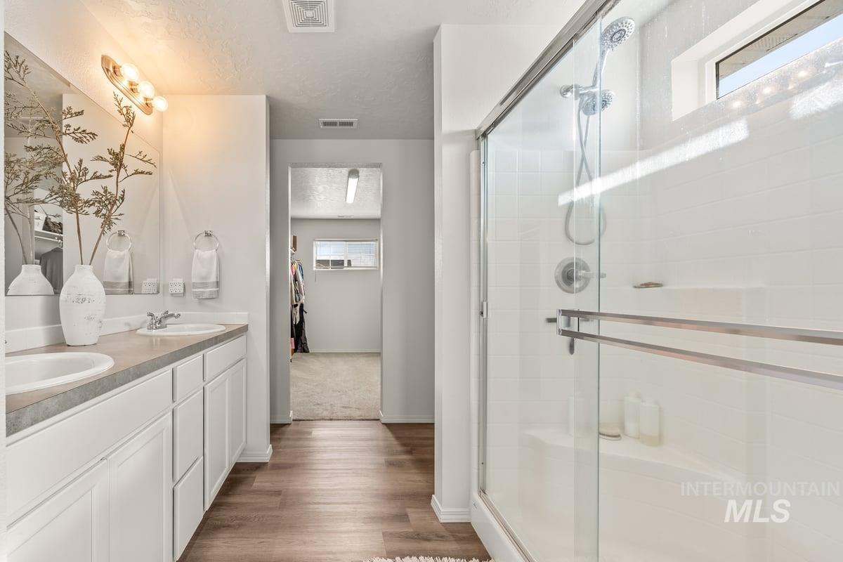 Full bathroom with a stall shower, double vanity, a textured ceiling, and dark wood-style flooring