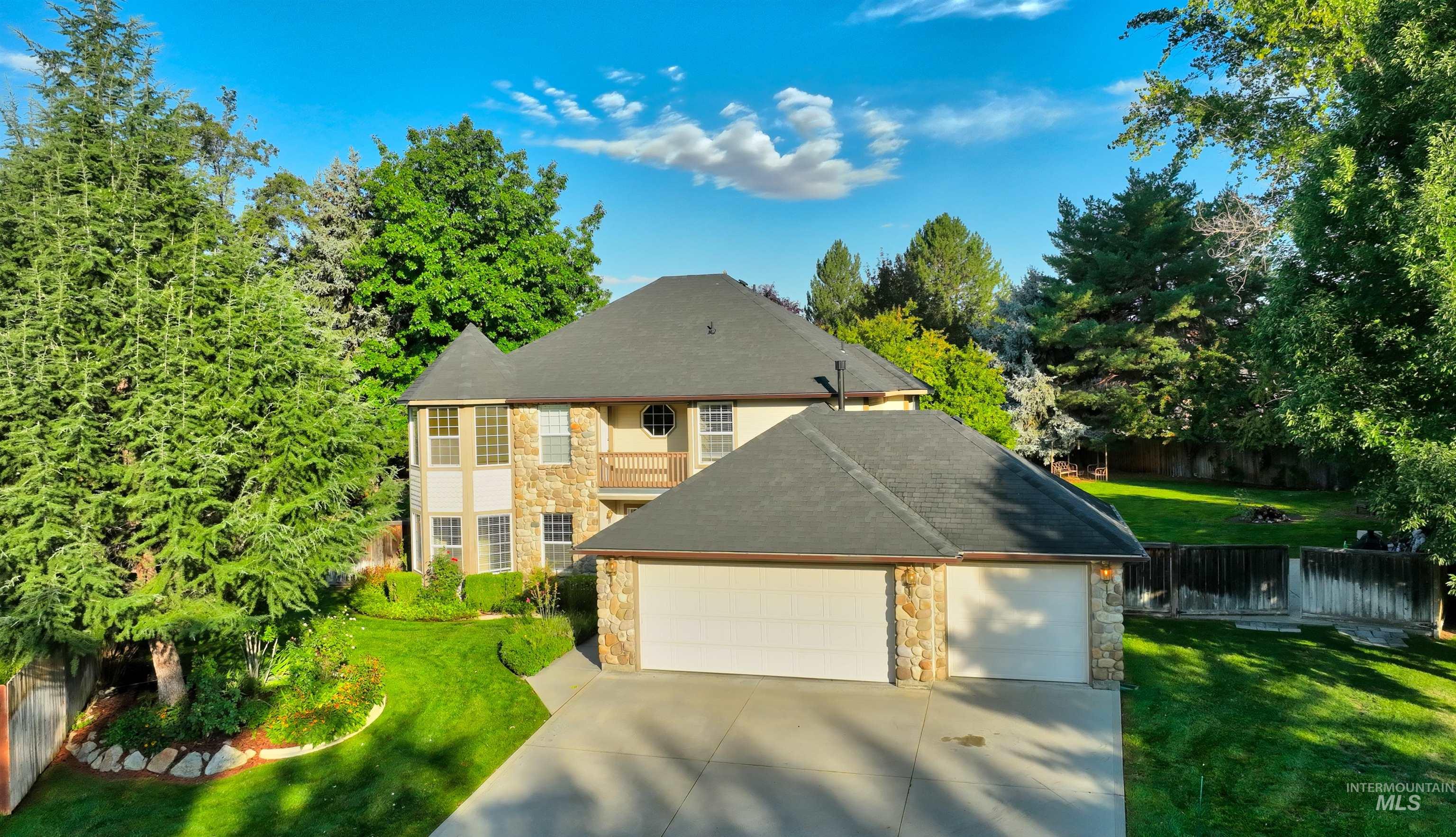 Traditional-style house featuring stone siding, a garage, a balcony, driveway, and a shingled roof