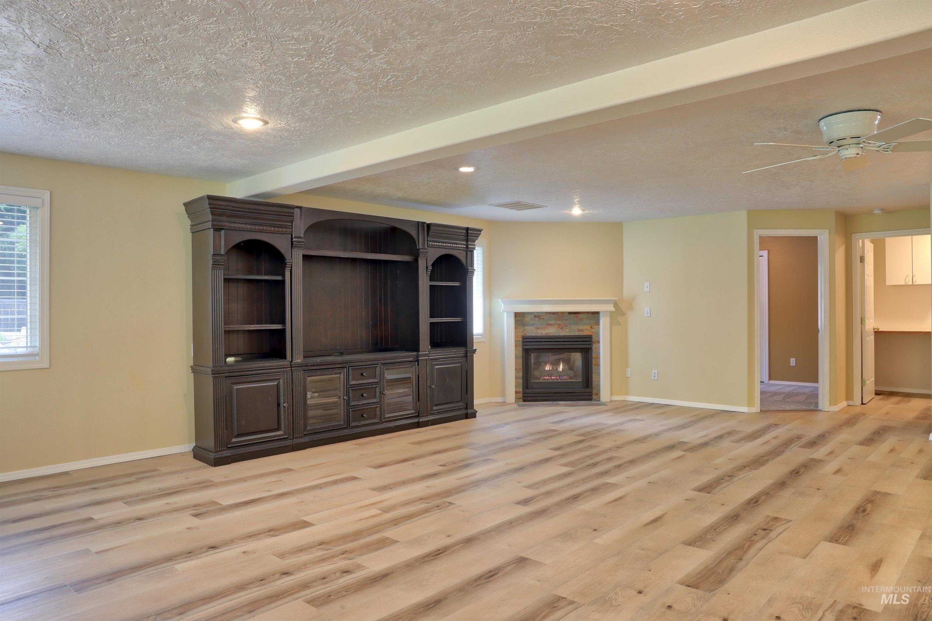Unfurnished living room featuring a glass covered fireplace, light wood finished floors, a textured ceiling, a ceiling fan, and recessed lighting