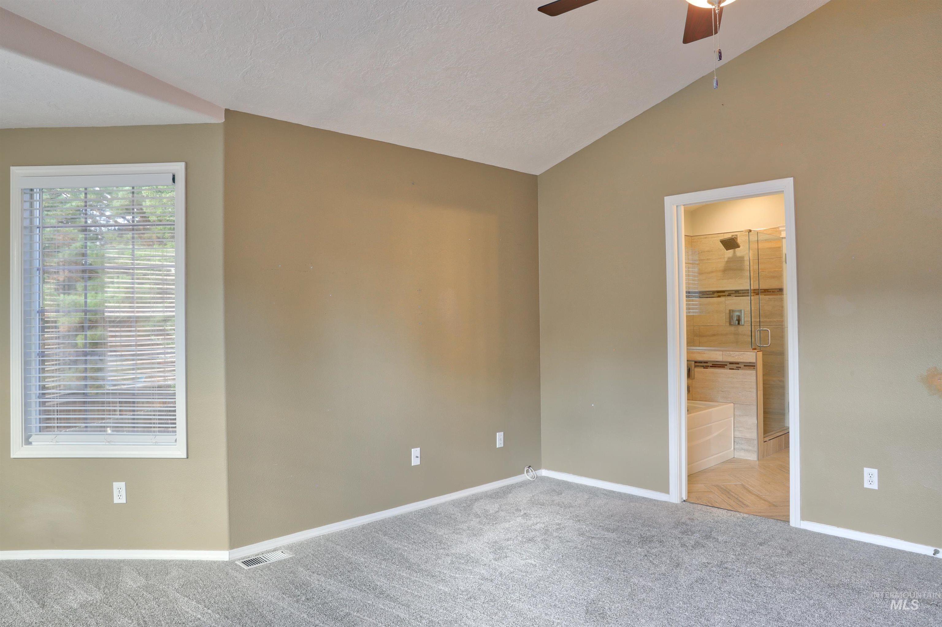 Unfurnished bedroom featuring vaulted ceiling, carpet floors, ceiling fan, ensuite bathroom, and a textured ceiling