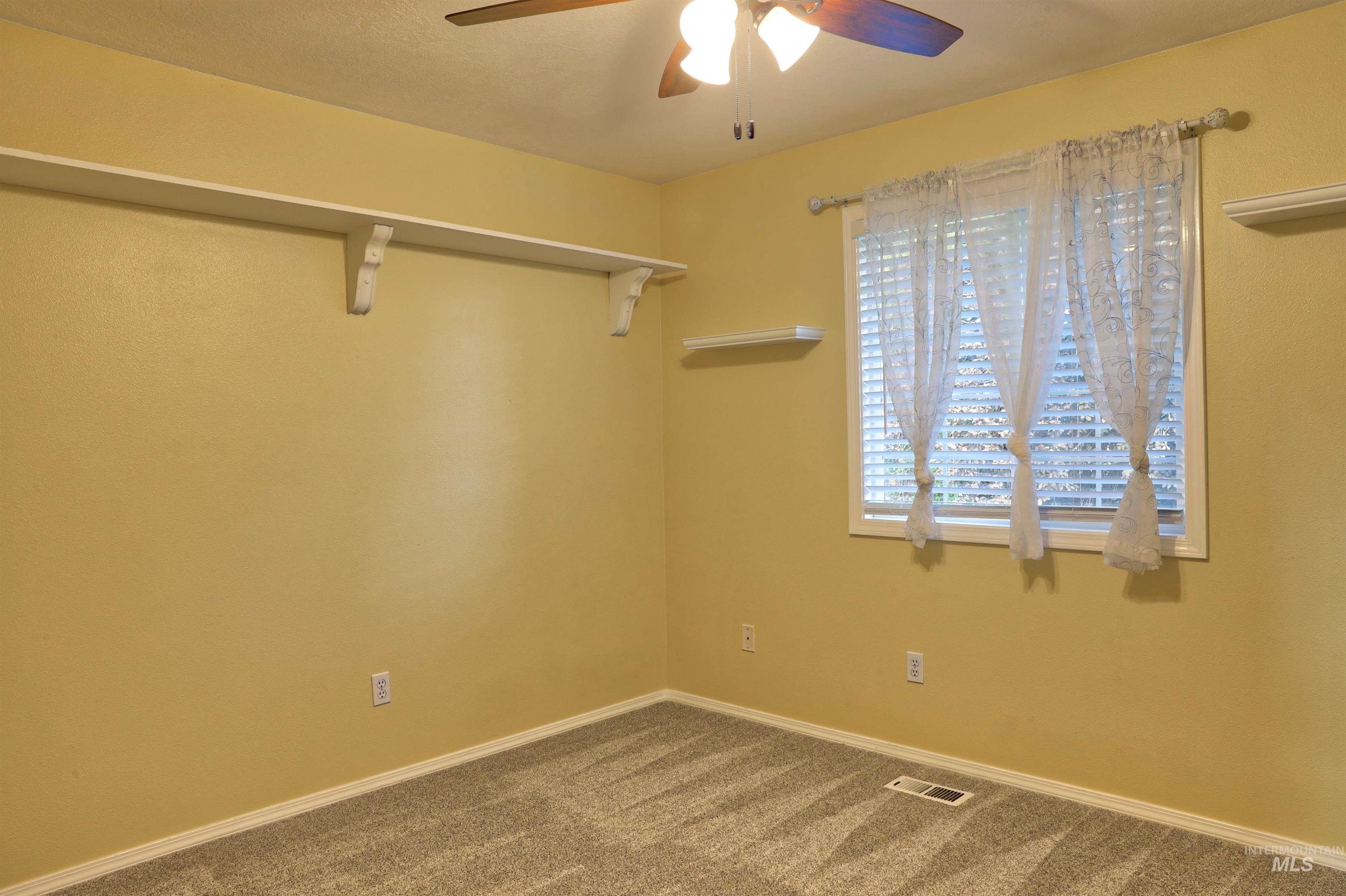 Carpeted spare room with a ceiling fan and baseboards