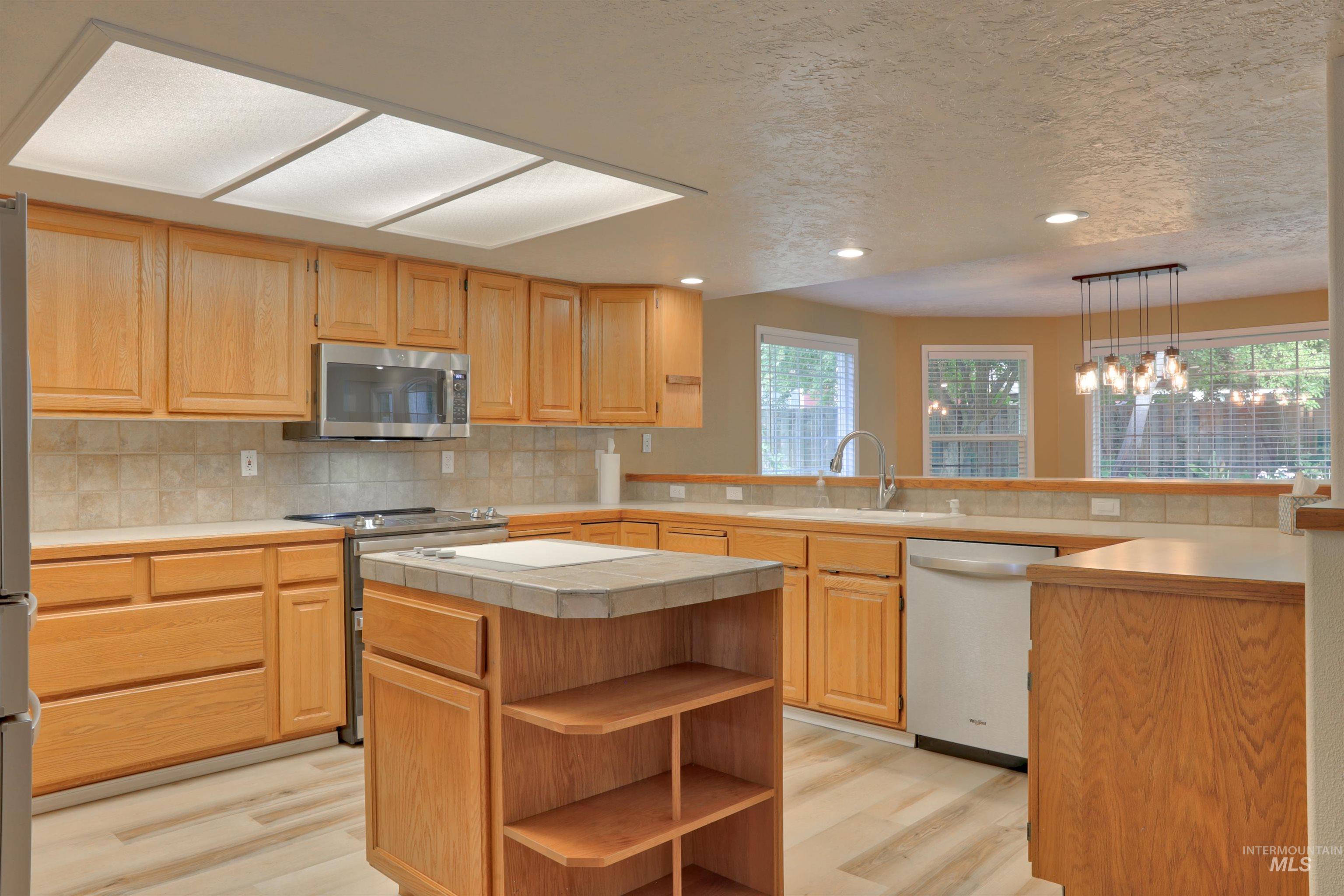 Kitchen with open shelves, a peninsula, tasteful backsplash, appliances with stainless steel finishes, and light wood finished floors