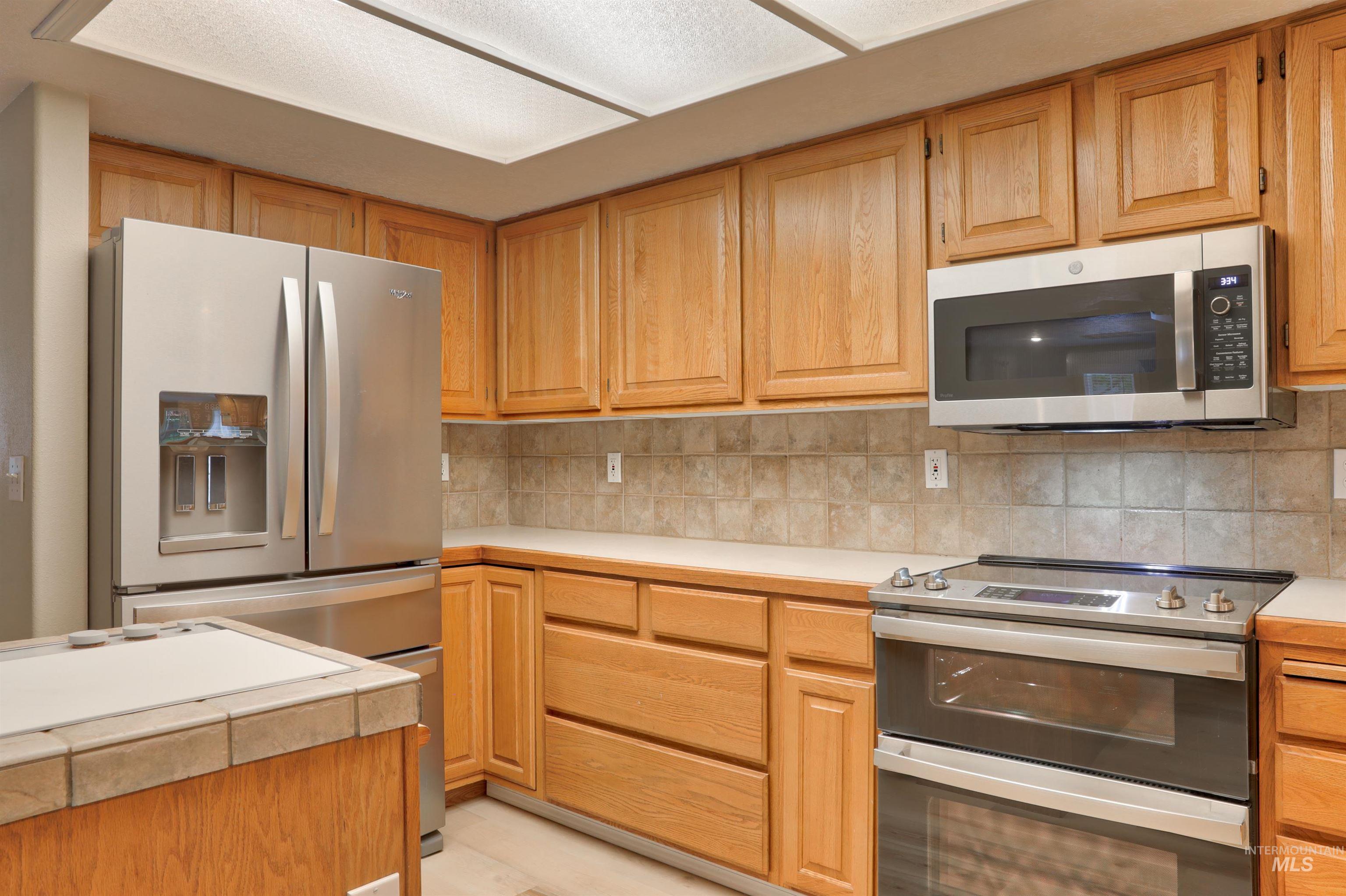 Kitchen featuring appliances with stainless steel finishes, light countertops, backsplash, and light brown cabinets