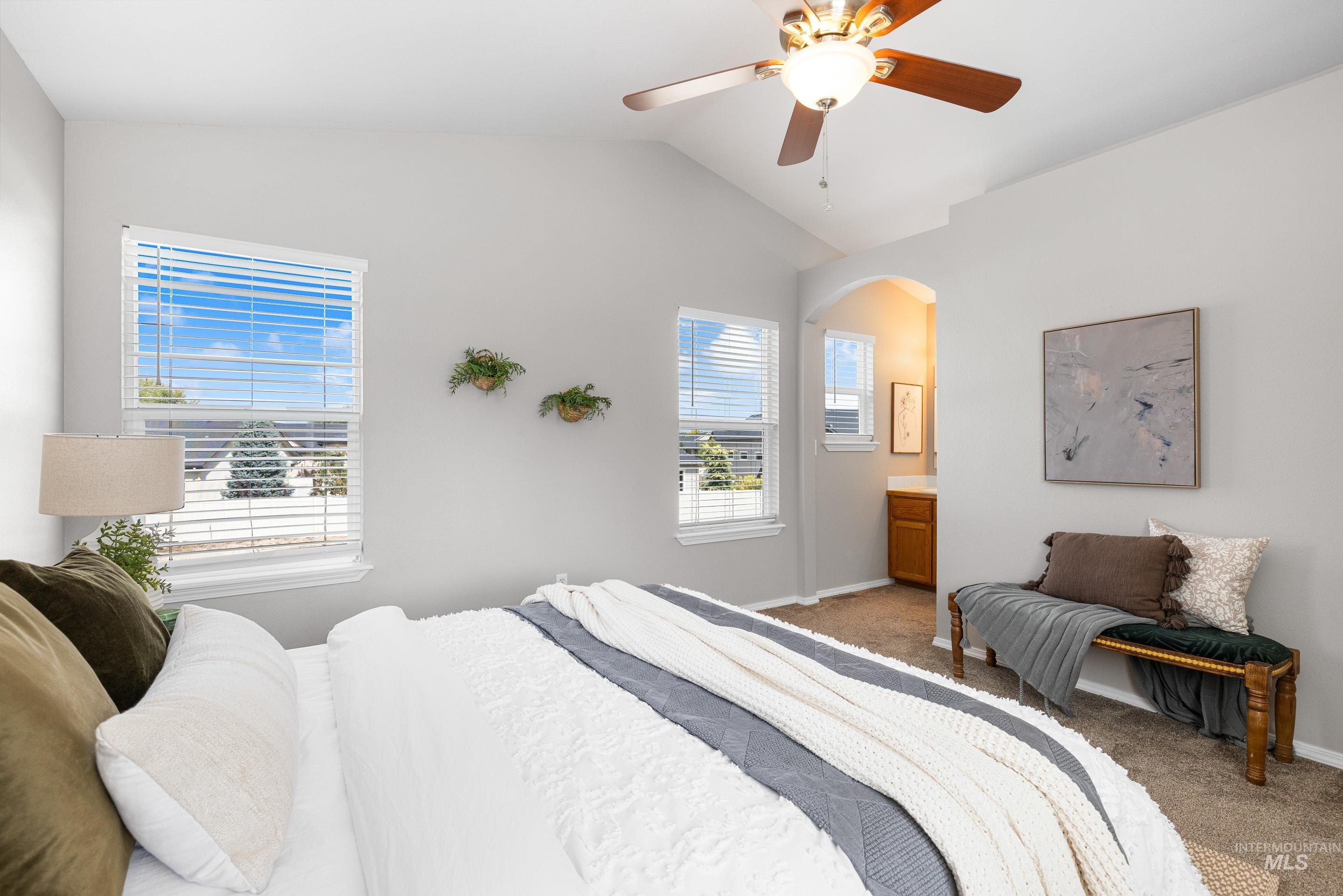Bedroom featuring carpet flooring, lofted ceiling, arched walkways, connected bathroom, and ceiling fan