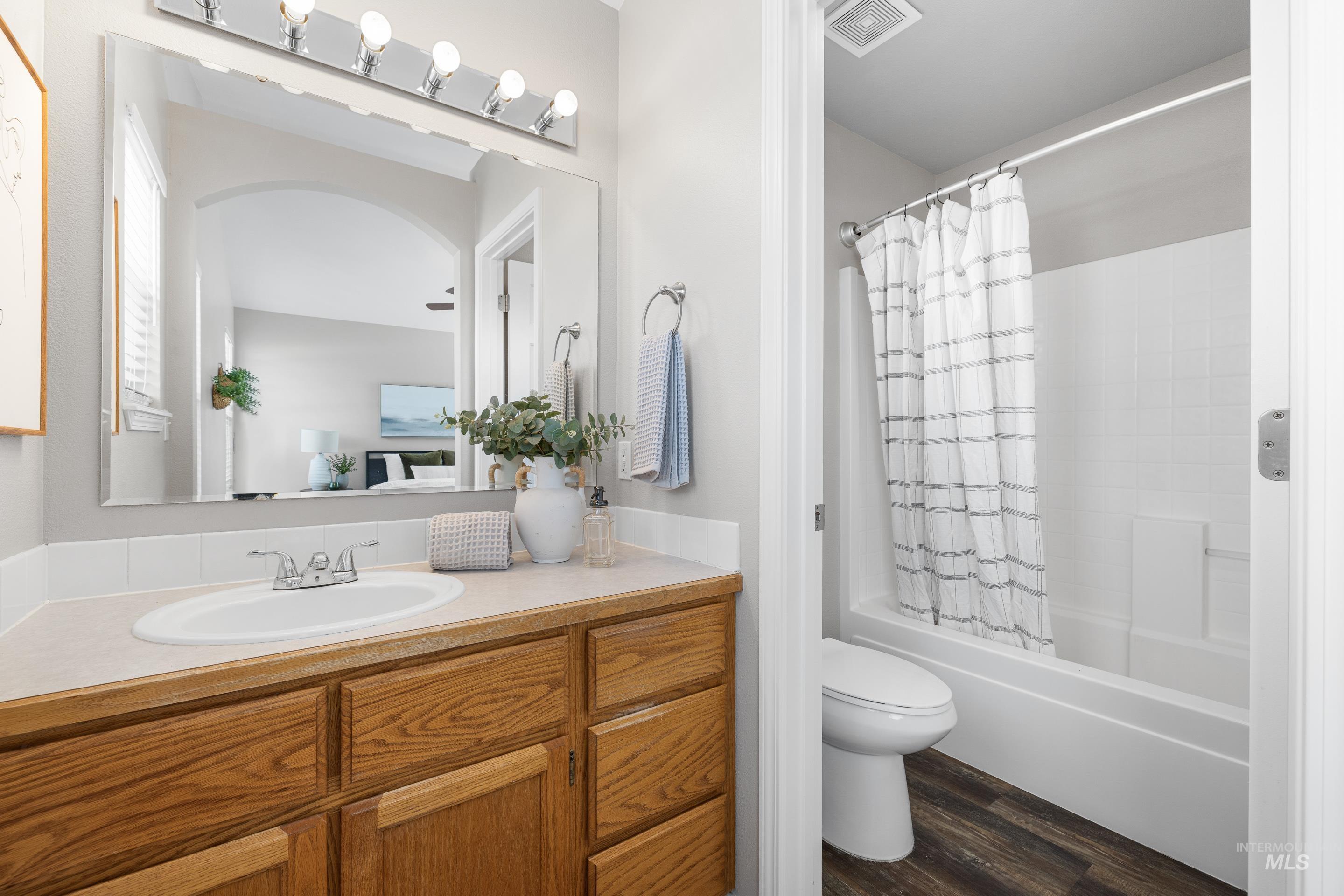 Full bathroom with shower / bath combination with curtain, vanity, and dark wood-style flooring