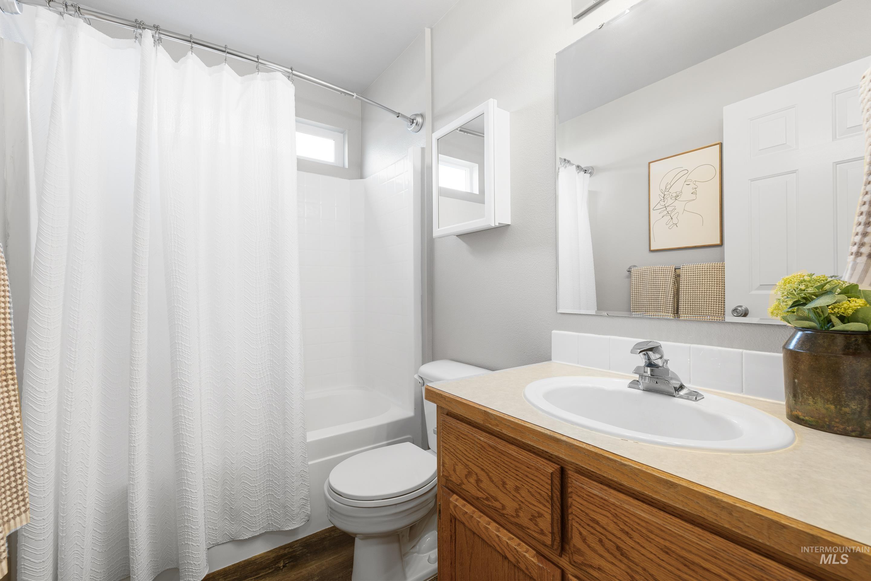 Bathroom featuring shower / bath combo with shower curtain, vanity, and dark wood-type flooring