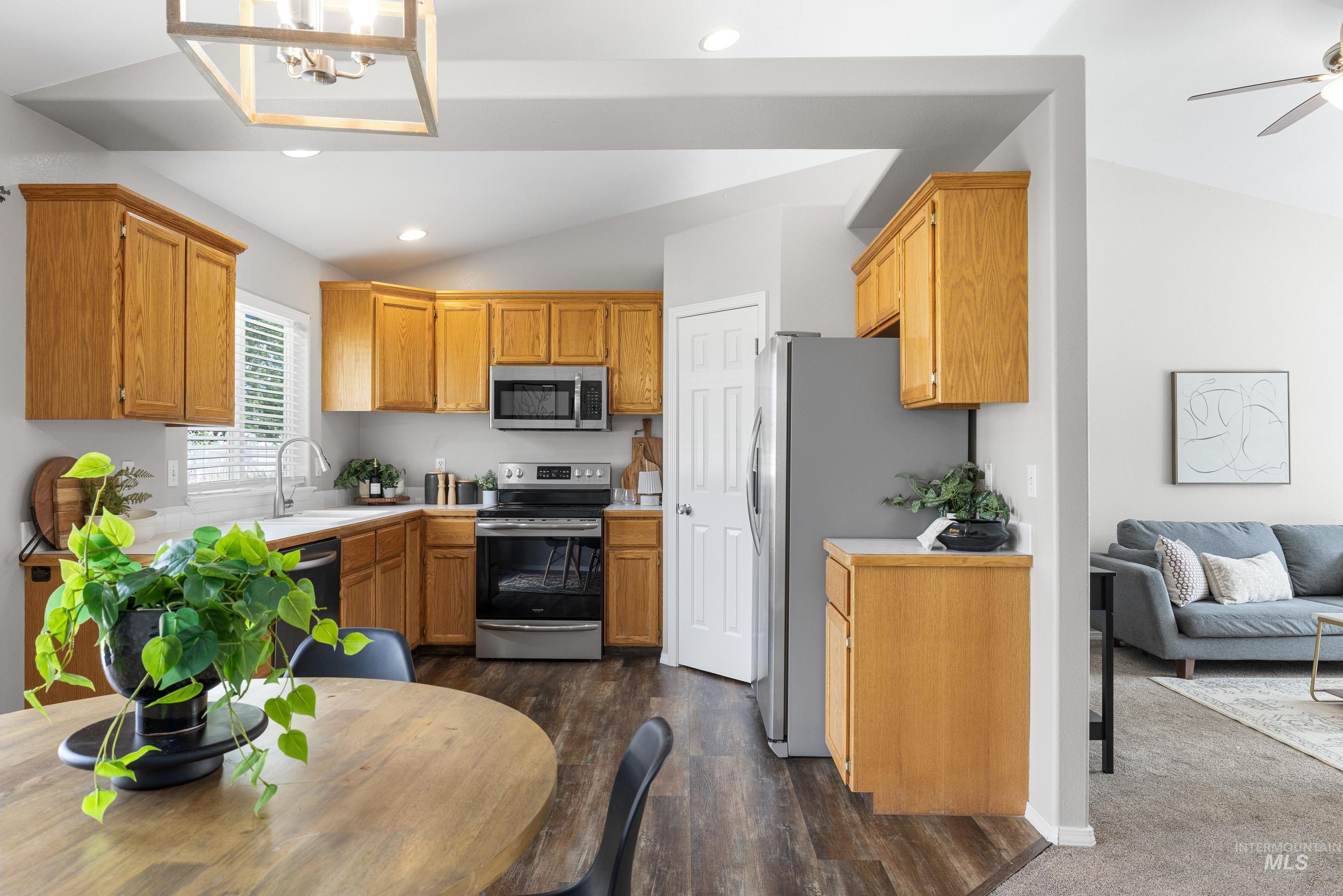 Kitchen with light countertops, stainless steel appliances, vaulted ceiling, brown cabinets, and dark wood-style flooring