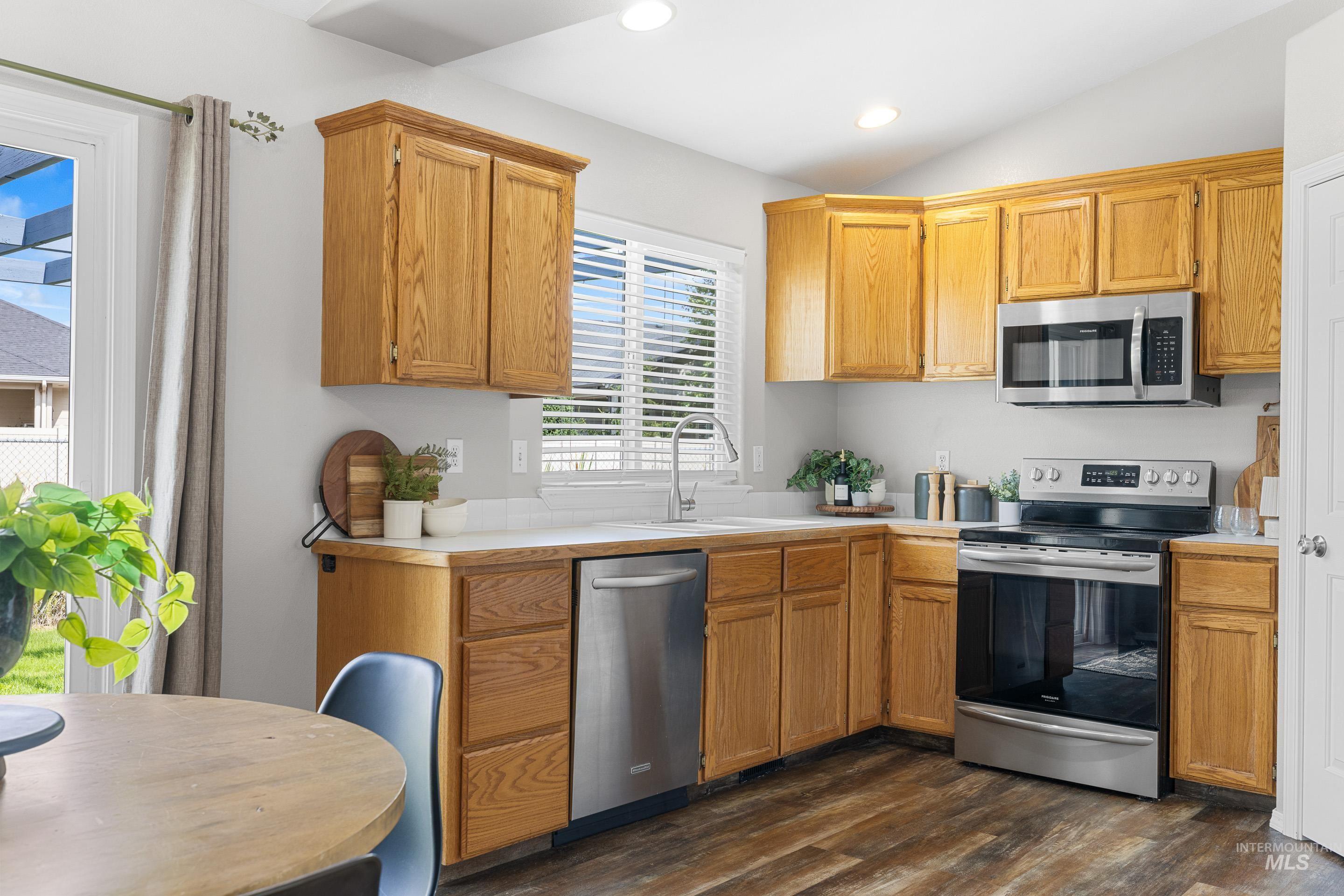 Kitchen featuring appliances with stainless steel finishes, light countertops, dark wood-style flooring, recessed lighting, and vaulted ceiling