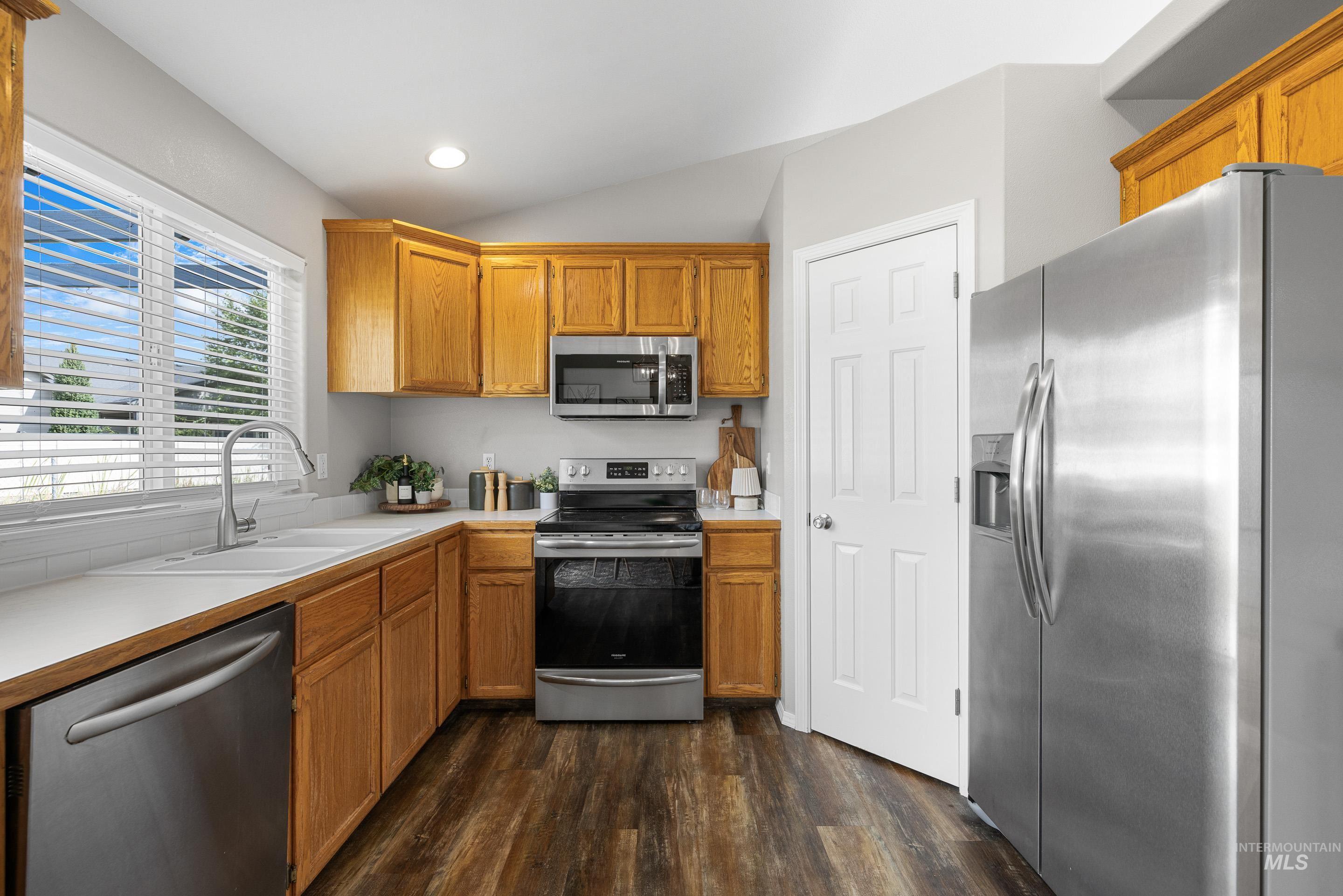 Kitchen with appliances with stainless steel finishes, light countertops, dark wood-style flooring, brown cabinets, and vaulted ceiling